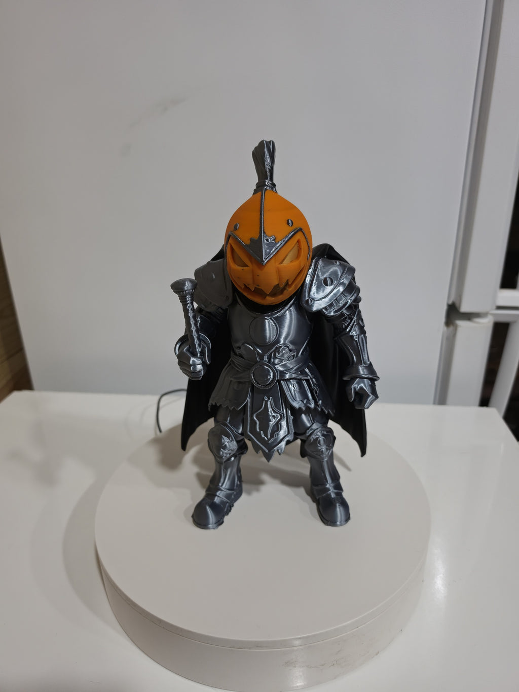 Actual silver-toned and orange Pumpkin Knight 3D print on display stand — wider front view.