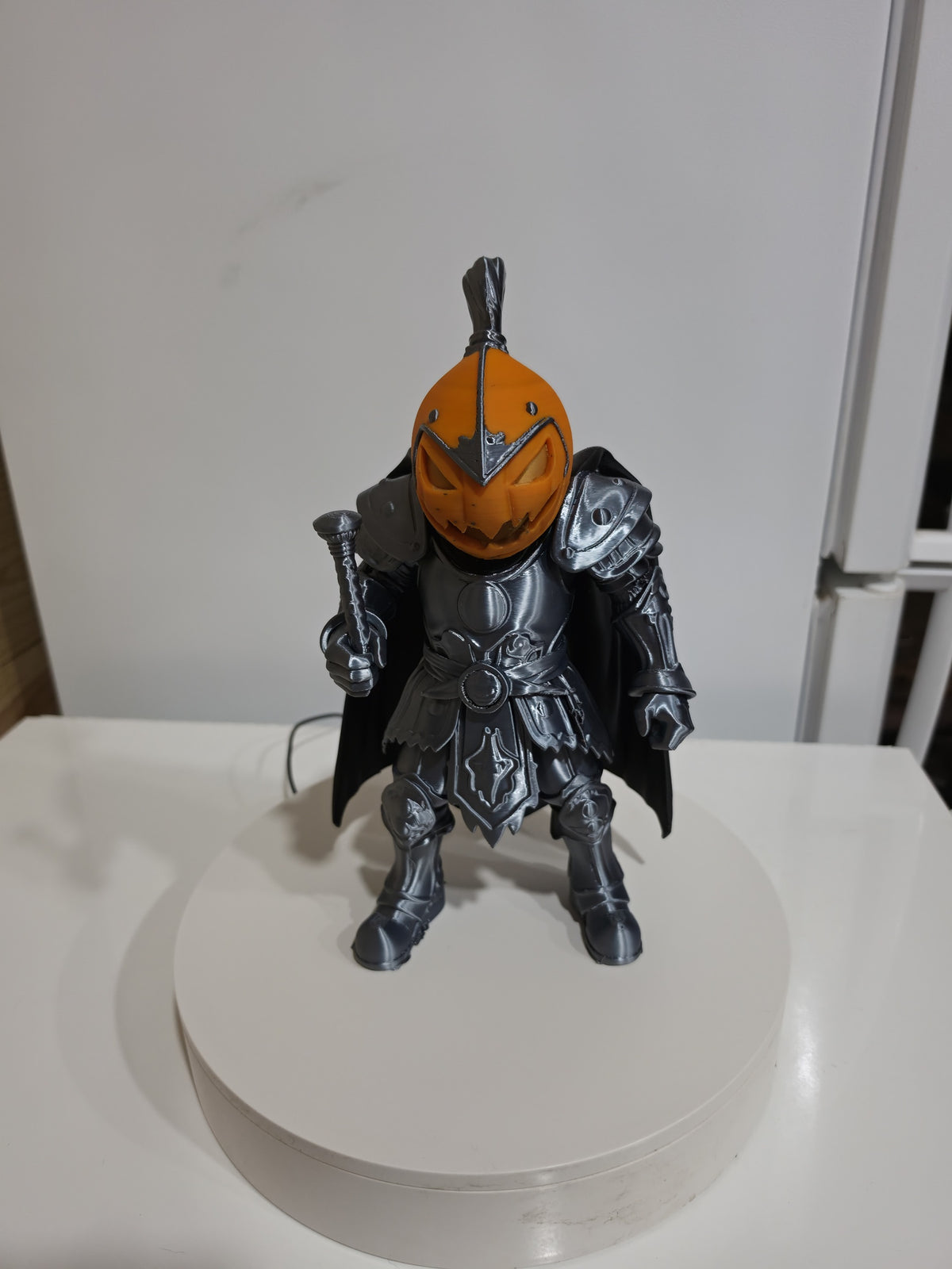 Actual silver-toned and orange Pumpkin Knight 3D print on display stand — wider front view.
